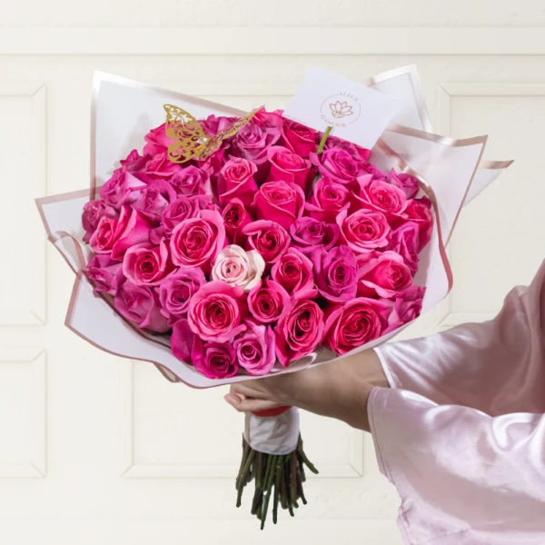 ramo buchón mediano de 50 rosas fucsias con papel coreano rosado que envuelve el ramo, en el ramo encuentras una mariposa dorada y una nota personalizada